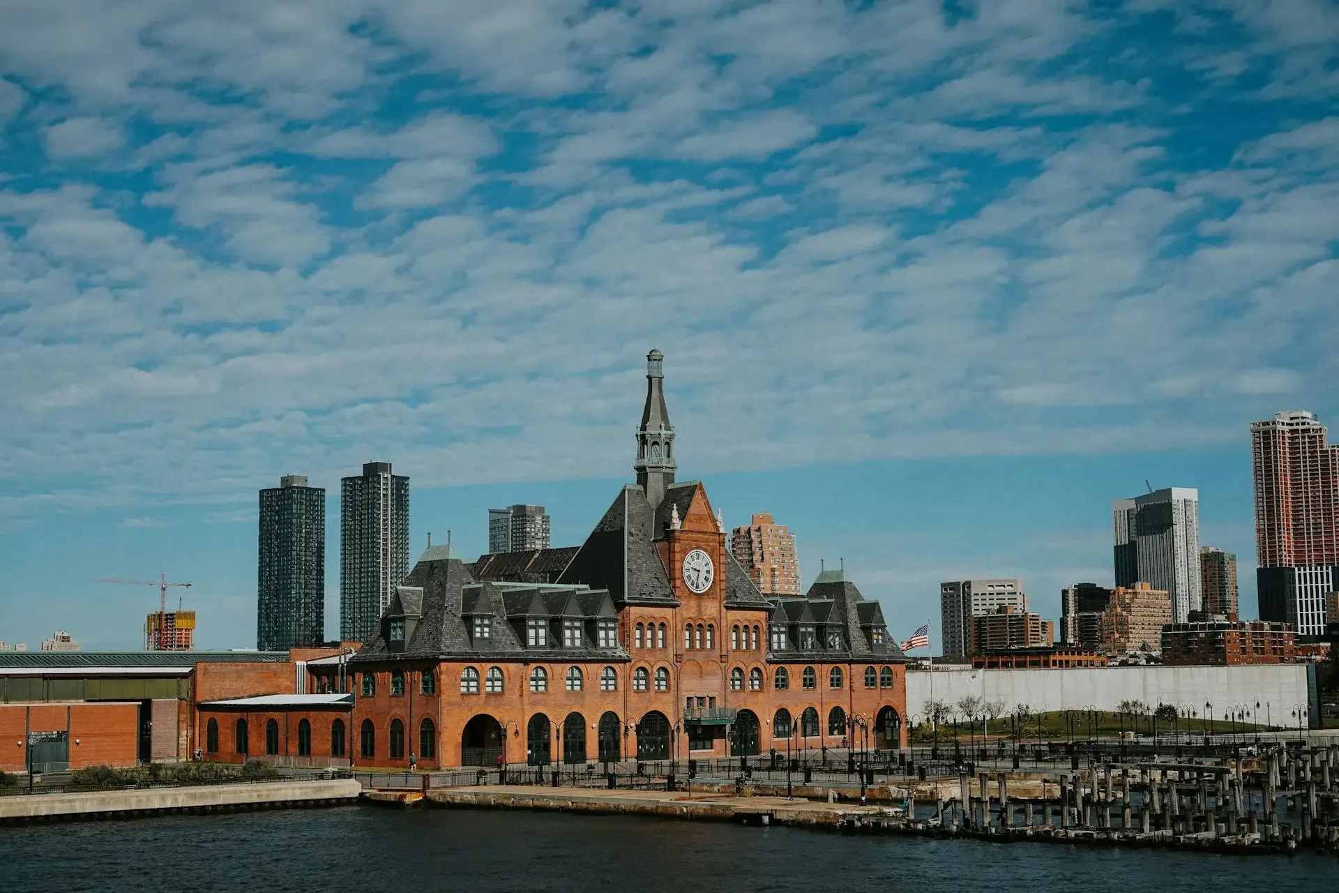 A large building with a clock tower stands beside a tranquil body of water, reflecting its grandeur